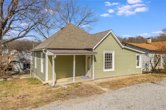 rear view of property with driveway and roof with shingles