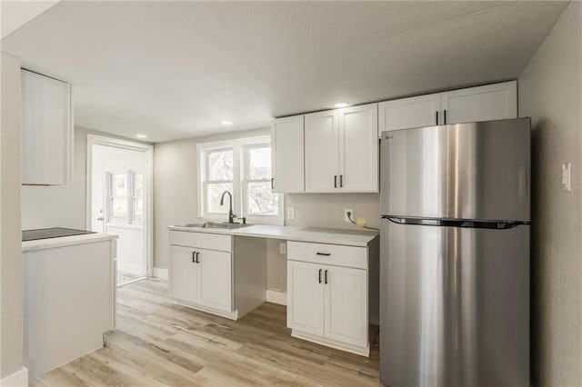 kitchen featuring light wood-style flooring, a sink, freestanding refrigerator, white cabinets, and light countertops