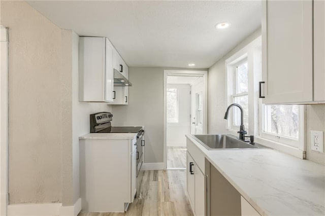 kitchen with under cabinet range hood, light wood-style flooring, range with electric stovetop, white cabinetry, and a sink