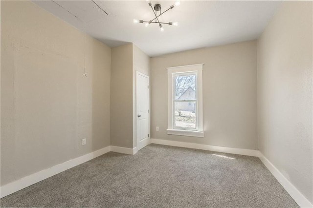 carpeted empty room with baseboards and a chandelier