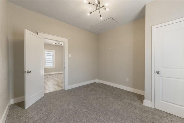 carpeted empty room featuring attic access and baseboards