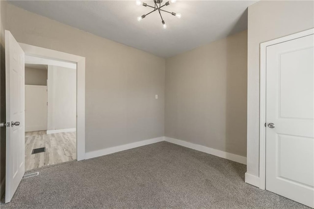 carpeted spare room featuring a chandelier, visible vents, and baseboards