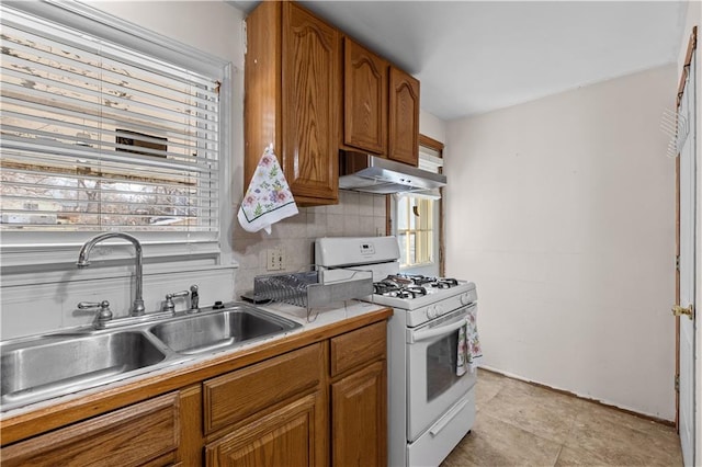 kitchen with white range with gas cooktop, brown cabinets, under cabinet range hood, a sink, and backsplash