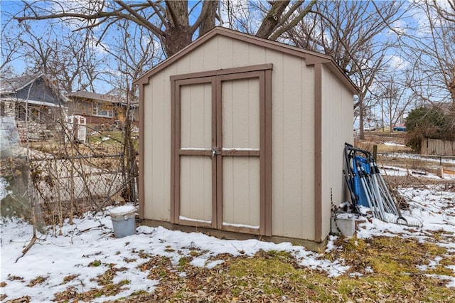 snow covered structure featuring fence, an outdoor structure, and a shed