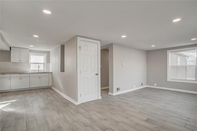 interior space featuring white cabinets, light wood-style floors, tasteful backsplash, and a sink