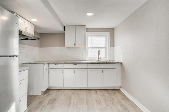 kitchen with a sink, under cabinet range hood, tasteful backsplash, freestanding refrigerator, and light wood finished floors