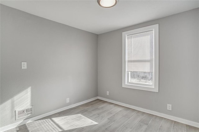 spare room with light wood-type flooring, visible vents, and baseboards