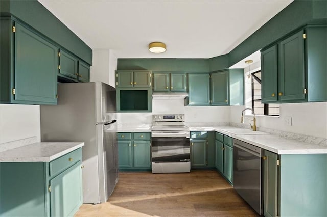 kitchen with a sink, under cabinet range hood, wood finished floors, stainless steel appliances, and light countertops