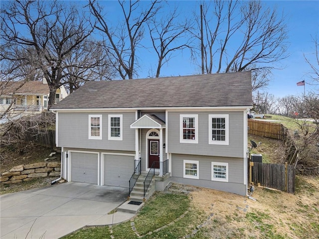 bi-level home with an attached garage, concrete driveway, and fence