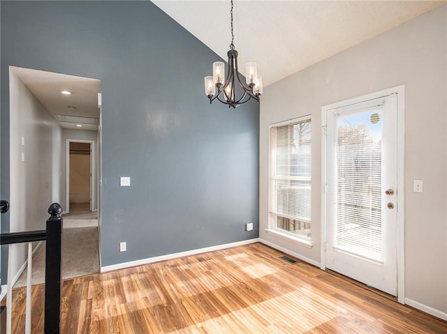 unfurnished dining area featuring a chandelier, visible vents, lofted ceiling, and wood finished floors