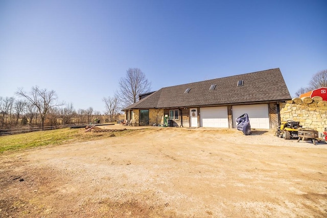 rear view of house with fence, a garage, dirt driveway, and a shingled roof