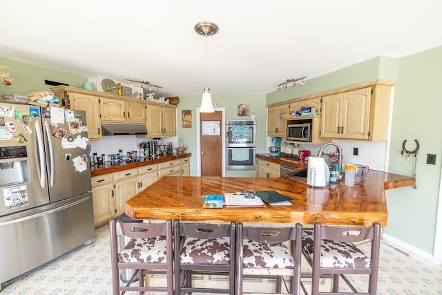 kitchen with under cabinet range hood, light floors, a peninsula, stainless steel appliances, and a sink