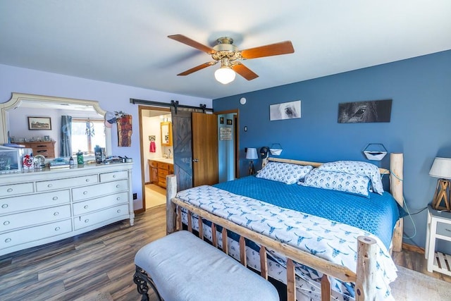 bedroom with a barn door, ensuite bathroom, wood finished floors, and a ceiling fan