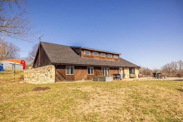 rear view of house with stone siding, a lawn, a patio, and a shingled roof