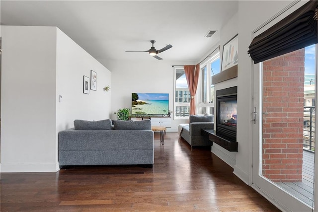 living room featuring visible vents, a ceiling fan, a glass covered fireplace, wood finished floors, and baseboards