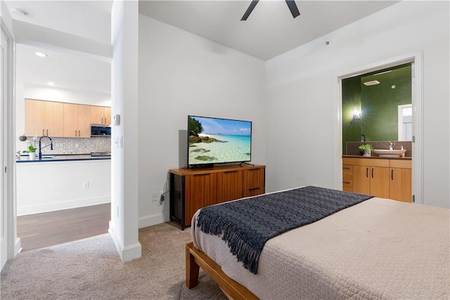 bedroom featuring light carpet, ensuite bath, baseboards, and a sink