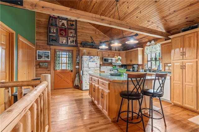 kitchen with beam ceiling, light wood-style flooring, stainless steel microwave, a kitchen island, and freestanding refrigerator