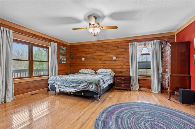 bedroom featuring ceiling fan, wooden walls, light wood finished floors, and a textured ceiling