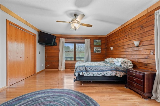 bedroom featuring wooden walls, light wood-style floors, a closet, and ceiling fan