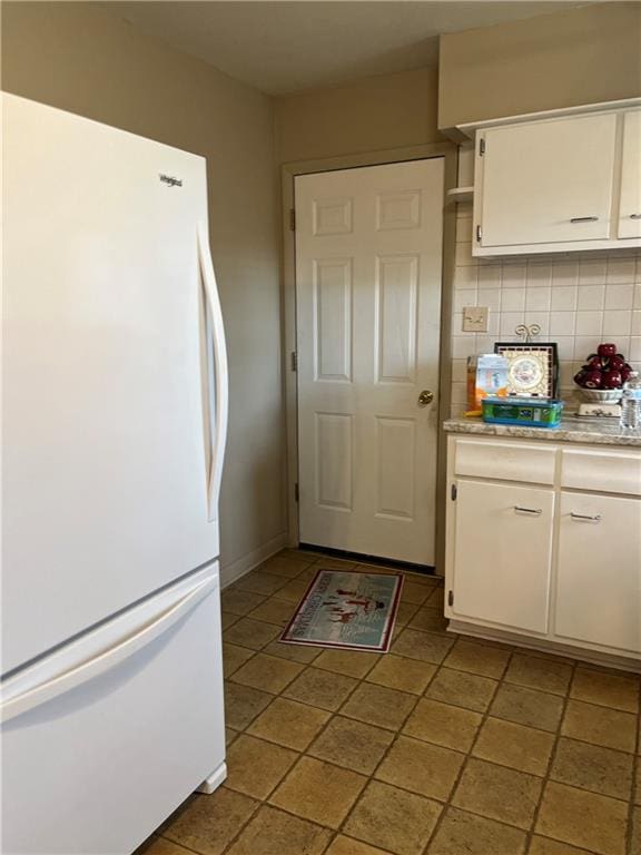 kitchen featuring baseboards, freestanding refrigerator, light countertops, white cabinets, and backsplash