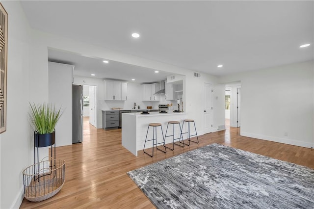 kitchen featuring light wood-style flooring, a sink, a peninsula, appliances with stainless steel finishes, and wall chimney exhaust hood