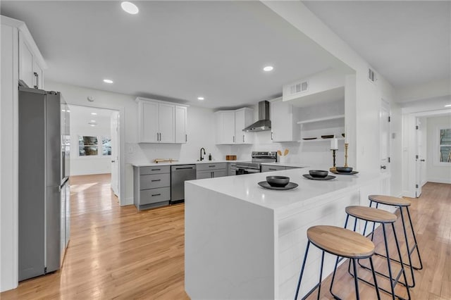 kitchen featuring visible vents, appliances with stainless steel finishes, a peninsula, wall chimney exhaust hood, and a sink