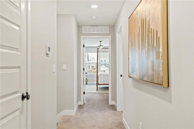 hallway with visible vents, baseboards, and light colored carpet