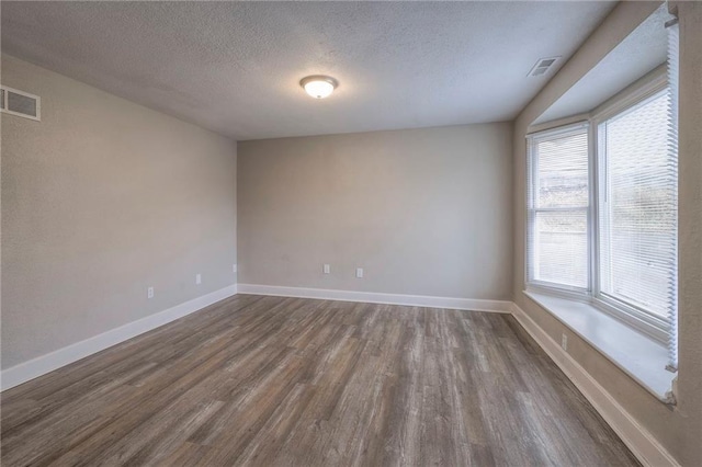 empty room with visible vents, baseboards, dark wood-type flooring, and a textured ceiling