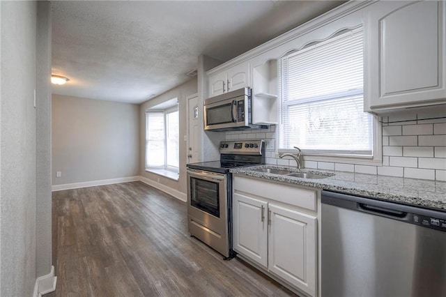 kitchen with tasteful backsplash, a sink, baseboards, appliances with stainless steel finishes, and dark wood-style flooring