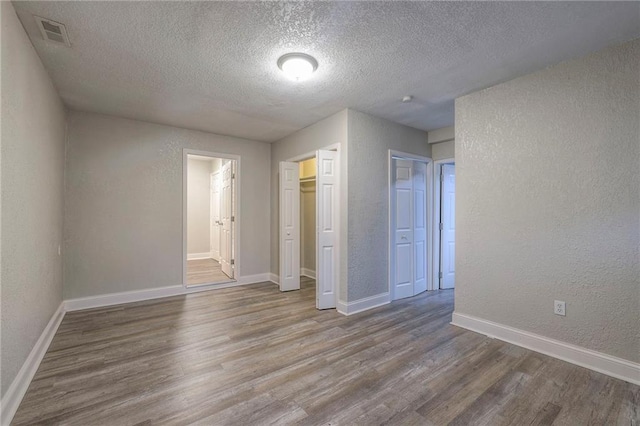 empty room featuring visible vents, baseboards, wood finished floors, and a textured wall