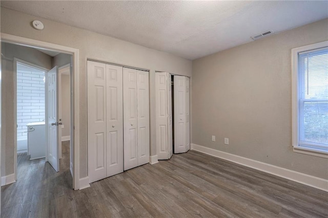 unfurnished bedroom featuring baseboards, visible vents, dark wood-type flooring, multiple closets, and a textured ceiling