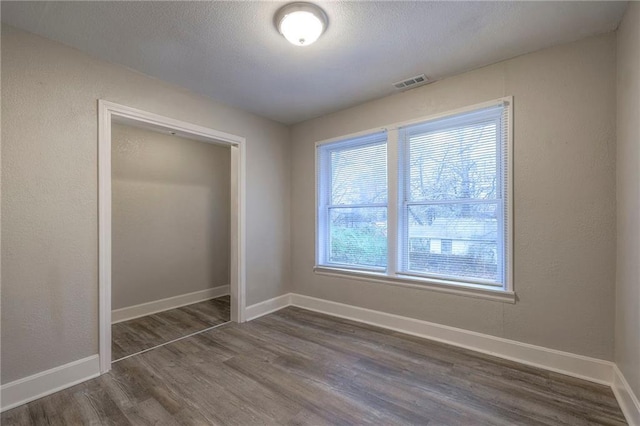 unfurnished bedroom featuring visible vents, a textured ceiling, dark wood finished floors, a closet, and baseboards