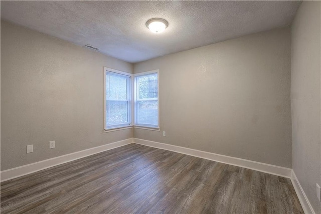 spare room featuring dark wood-type flooring, visible vents, baseboards, and a textured ceiling