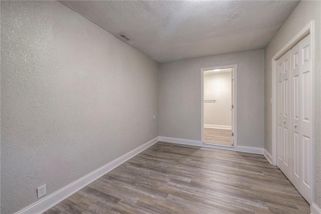 unfurnished bedroom with visible vents, baseboards, wood finished floors, a textured wall, and a closet