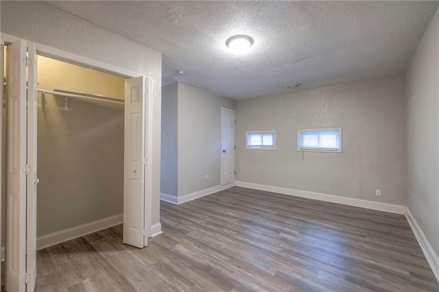 unfurnished bedroom featuring a textured ceiling, wood finished floors, a closet, baseboards, and a textured wall