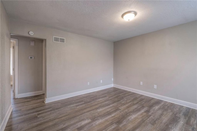 empty room featuring dark wood finished floors, baseboards, visible vents, and a textured ceiling