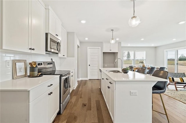 kitchen with a kitchen bar, a sink, wood finished floors, stainless steel appliances, and white cabinets