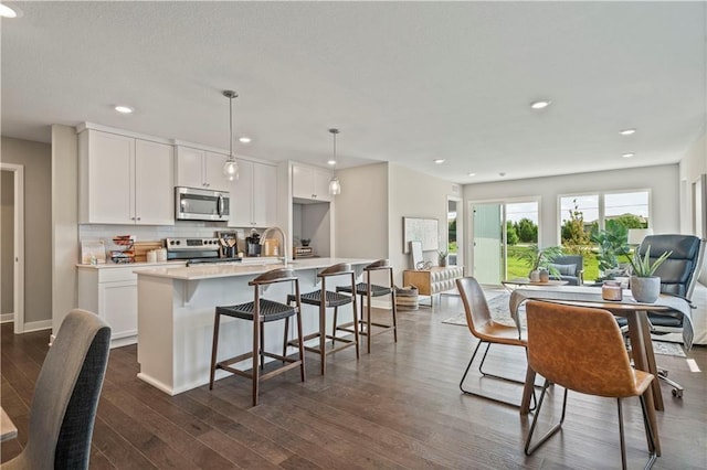 kitchen with a center island with sink, stainless steel appliances, dark wood-type flooring, tasteful backsplash, and open floor plan