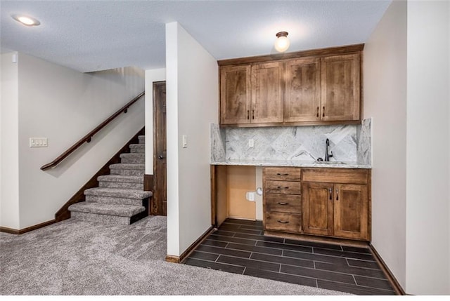 kitchen featuring dark wood-style floors, brown cabinetry, baseboards, a sink, and decorative backsplash