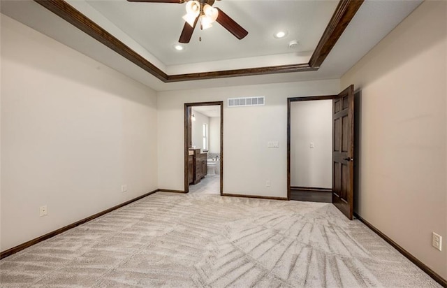 unfurnished bedroom featuring visible vents, baseboards, light carpet, ensuite bathroom, and a raised ceiling