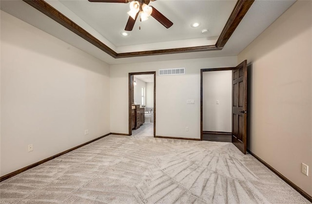 unfurnished bedroom with visible vents, baseboards, light colored carpet, ensuite bath, and a raised ceiling