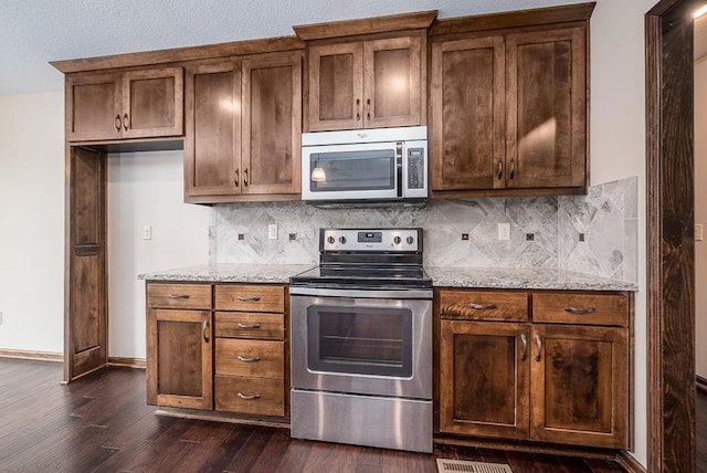 kitchen with backsplash, baseboards, light stone counters, stainless steel appliances, and dark wood-style flooring