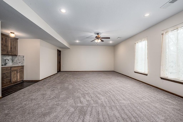 unfurnished living room featuring baseboards, visible vents, dark colored carpet, and ceiling fan