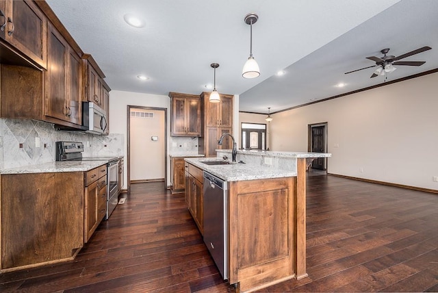 kitchen with dark wood-style flooring, appliances with stainless steel finishes, light stone countertops, and a sink