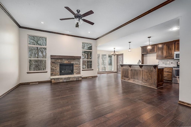 unfurnished living room with ceiling fan with notable chandelier, a sink, dark wood finished floors, a stone fireplace, and baseboards