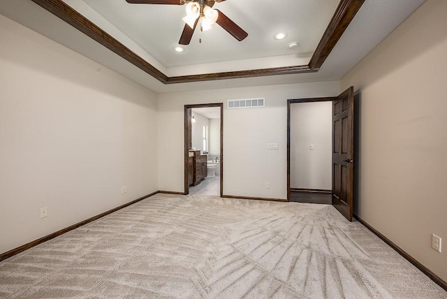 unfurnished bedroom featuring visible vents, baseboards, light colored carpet, a tray ceiling, and ensuite bath