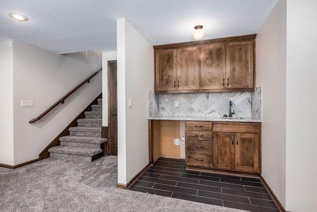 kitchen with baseboards, wood finish floors, a sink, a textured ceiling, and backsplash