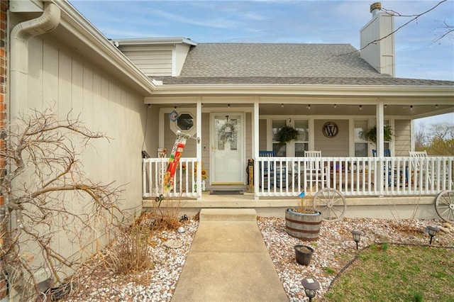 entrance to property with a chimney, covered porch, and a shingled roof