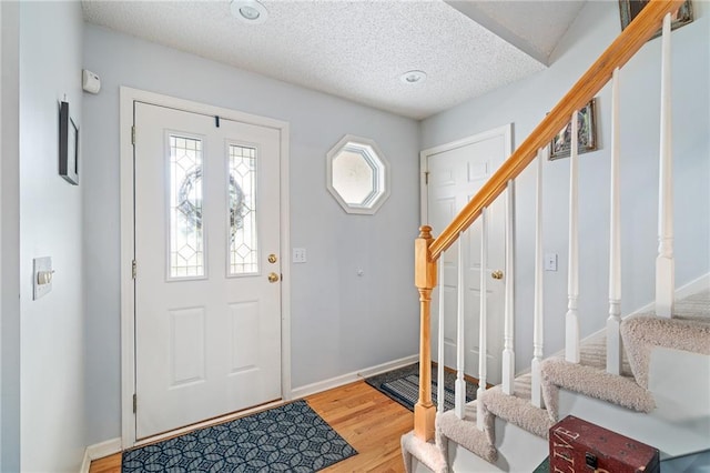 foyer featuring light wood-type flooring, baseboards, a textured ceiling, and stairs