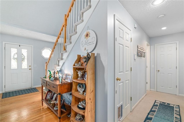 foyer entrance with baseboards, light wood-type flooring, stairs, recessed lighting, and a textured ceiling